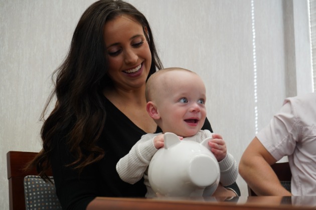 A young mother with her child on her lap holding a piggy bank. 