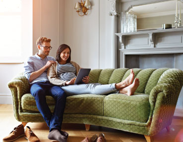 a couple sitting on a couch looking at a tablet